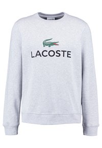 Felpa grigia con maniche lunghe, con un grande logo di coccodrillo verde e la scritta "LACOSTE" in nero sul petto. Tessuto morbido.