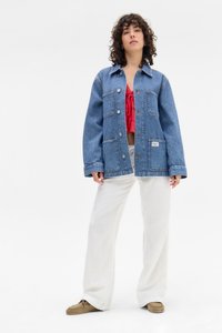 Denim jakna plave pruge s velikim džepovima, dugmadi sprijeda i ležernim krojem, uparena s crvenim crop topom i bijelim širokim hlačama.