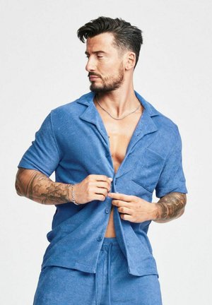 Camicia azzurra a maniche corte con bottoni, texture morbida, taschino sul petto, pantaloni corti coordinati, vestibilità rilassata, progettata per comfort e abbigliamento casual.