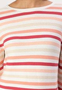 Striped knit sweater featuring horizontal lines in shades of coral, peach, cream, and burgundy; soft texture with a crew neckline.