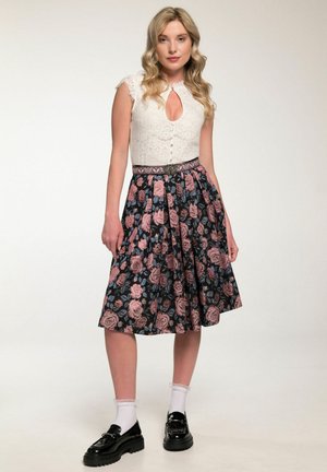 Weißes Spitzenoberteil mit Ausschnitt, kombiniert mit einem schwarzen Rock mit Blumenmuster, der rosa und blaue Rosen zeigt. Glänzende schwarze Schuhe und weiße Socken.