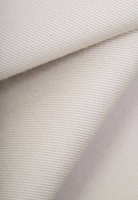 Beige canvas fabric folded to show texture and weave. The surface is smooth with a subtle sheen, suited for textiles or upholstery.