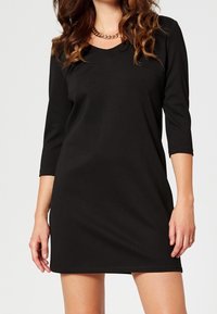 Svart, knälång klänning gjord av slätt tyg, med V-ringning och trekvartsärmar. Enkelt design utan synliga mönster.