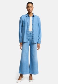 Jasnoniebieska koszula denimowa w zestawie z jasnoniebieskimi spodniami o wysokim stanie i szerokich nogawkach. Posiada kieszeń na piersi oraz zapinanie na guziki z przodu.