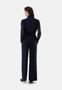 Marine-farbenes Zweiteiler-Outfit mit einem figurbetonten Oberteil mit Spitzensäumen, hoch taillierten, weiten Hosen und einem Kragen. Getragen mit schwarzen High Heels.