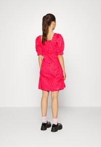 Vestido de mangas bufantes, até ao joelho, em rosa brilhante com estampado floral. Apresenta um decote quadrado e uma bainha ampla. Usado com sapatos chunky e meias.