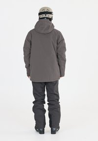 Grå udendørsjakke med hætte, parret med mørke bukser og sorte sko. Designet har en afslappet pasform og minimalistisk stil.