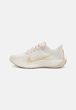 Chaussure de course Nike ZoomX beige avec tige en mesh, design à lacets, semelle rembourrée et logo Nike swoosh doré sur le côté.