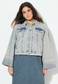 Beskuren denimjacka i ljusblått med två bröstfickor, slitna ärmar och en blekt tvätt. Knäppning fram och spetsig krage.