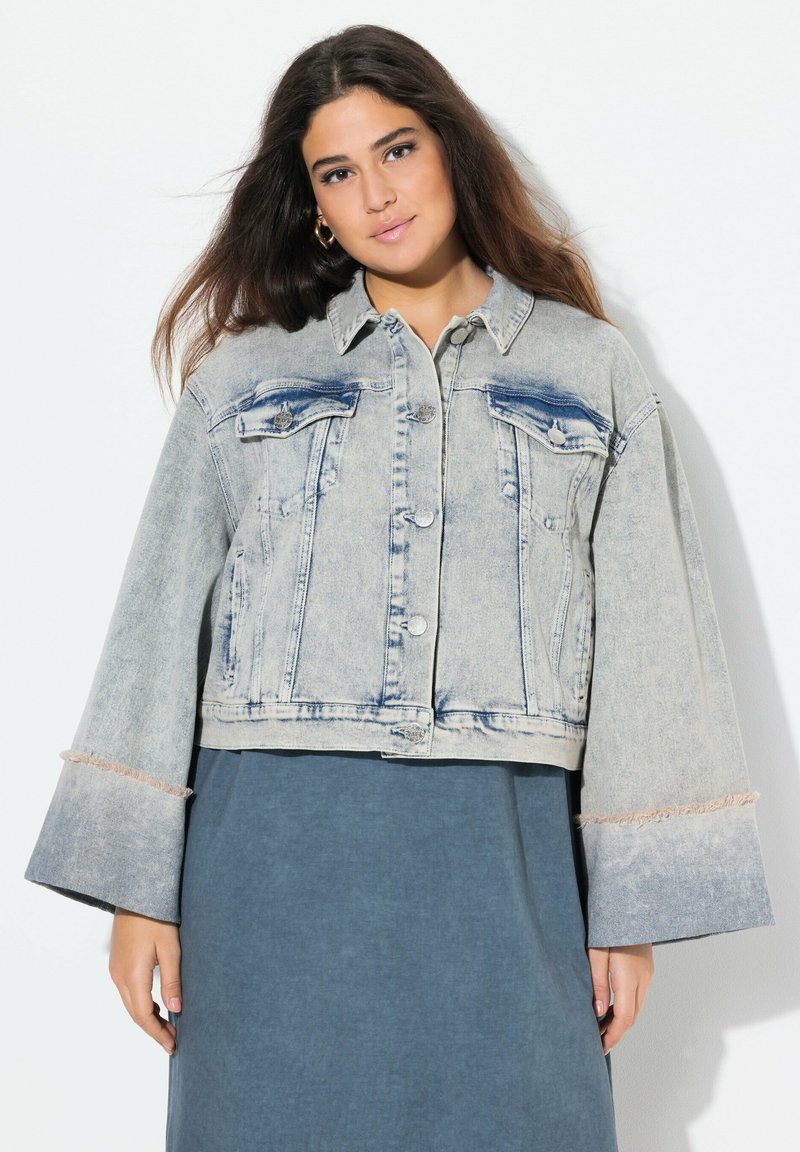 Beskuren denimjacka i ljusblått med två bröstfickor, slitna ärmar och en blekt tvätt. Knäppning fram och spetsig krage.