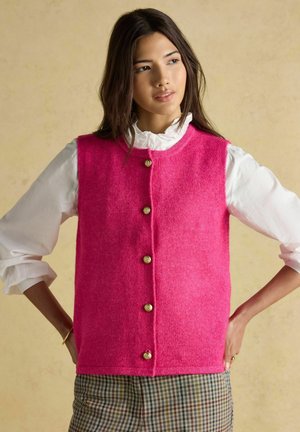 Fuchsia-farbene Wollweste mit rundem Ausschnitt, ausgestattet mit goldenen Knöpfen vorne, kombiniert mit einem weißen Rüschenhemd und karierten Hosen.