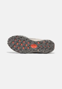 Suela de zapatilla de trail running con un diseño de goma gris agresivo, con acentos naranjas. Texturizada para un mejor agarre en diversos terrenos.