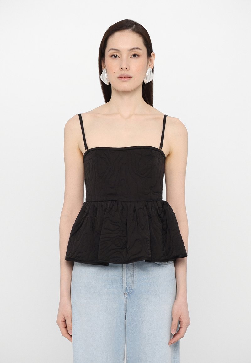 Black peplum top with thin spaghetti straps, textured fabric, and a structured bodice. Paired with light blue high-waisted jeans.