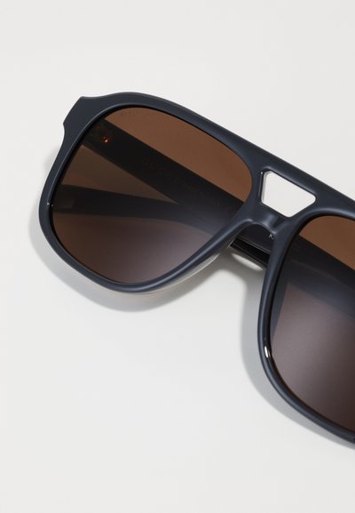 Gafas de sol Gucci con montura de plástico azul oscuro y lentes de gradiente marrón. Presentan un diseño de corte único cerca de las bisagras.