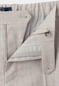 Ceinture de pantalon gris clair avec fermeture par bouton, braguette zippée et détails de couture visibles sur la boutonnière.