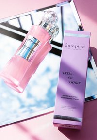 Rosa Glasflasche mit einem kristallähnlichen Verschluss, beschriftet mit "âme pure PEELS SO GOOD", neben einem Lavendelkarton mit ähnlicher Markenidentität.