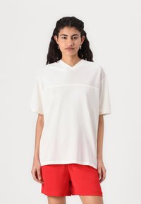 Chemise blanche en maille à manches courtes avec un col en V, corps texturé et panneau supérieur uni. Associée à un short rouge pour créer un contraste.