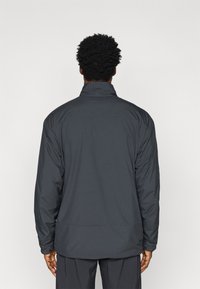 Veste légère gris foncé avec un col montant, une coupe décontractée et des poignets élastiques. Fabriquée en tissu lisse, avec un design simple sans ornements.