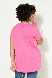 Fuchsia short-sleeve t-shirt with a rounded hem and soft texture, paired with blue denim jeans showing a distressed pattern.