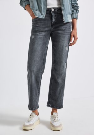 Grijze versleten jeans met een relaxte pasvorm, voorzien van versleten patches en een rechte pijp. Gecombineerd met witte sneakers en een lichtblauwe jas.