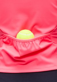 Μπάλα του τένις τοποθετημένη στην πίσω τσέπη ενός φωτεινού ροζ αθλητικού πουκάμισου Björn Borg, με σκοτεινό φόντο.