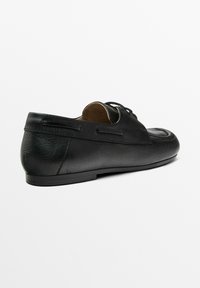 Chaussure en cuir noir avec un bout rond, profil bas, design à lacets, finition texturée et coutures minimalistes à l'arrière.