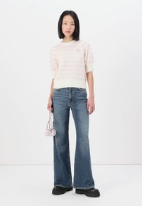 Strickpullover in Creme mit rosa Streifen, kombiniert mit weit geschnittenen blauen Jeans. Die Accessoires umfassen eine kleine rosa Tasche und klobige schwarze Schuhe.