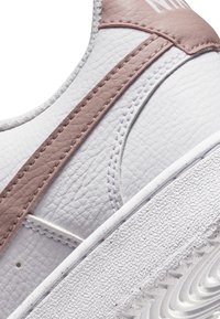 Sneaker sintetica bianca con superficie texturizzata, dettagli in pelle rosa e cuciture curve. La suola presenta un motivo scanalato.