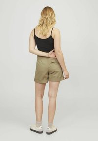 Pantaloni corti khaki con orlo arrotolato, realizzati in misto cotone, presentano una tasca posteriore e sono abbinati a una canotta nera e scarpe da ginnastica casual.