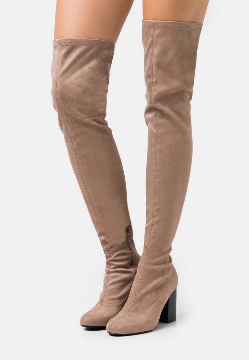 Bottes hautes beige en daim doux, avec un talon bloc, une silhouette élégante et une fermeture éclair latérale pour un enfilage facile.