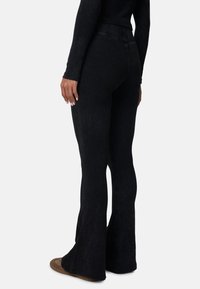 Zwarte flared corduroy broek met een hoge taille, voorzien van verticale ribbelstructuur en een accent nabij de tailleband. Textuur afwerking van de stof.