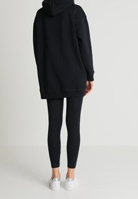 Czarna, oversize bluza z kapturem, zestawiona z czarnymi legginsami i białymi trampkami z metalicznymi akcentami. Prosty, luźny krój.