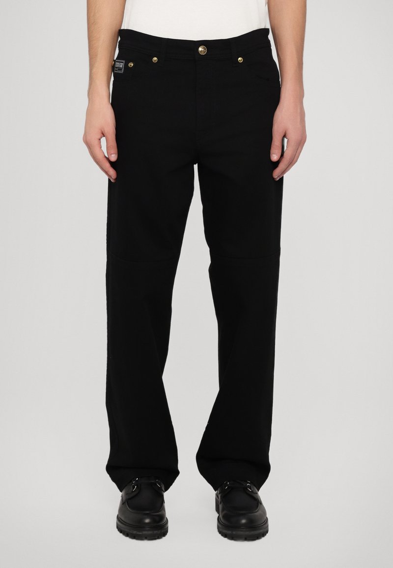 Pantalones de mezclilla negros con un corte relajado, que presentan herrajes en tono dorado, un diseño clásico de cinco bolsillos y piernas ligeramente ajustadas.