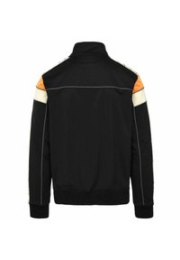Chaqueta deportiva negra con un alto cuello, que presenta detalles en naranja y crema en los hombros, ribete blanco y puños y dobladillo acanalados.