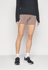 Pantalones cortos atléticos beige con un diseño ajustado, bolsillos laterales, combinados con una camiseta negra de manga larga y zapatillas de correr negras, con calcetines blancos.