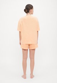 Souprava loungewear v broskvové barvě obsahuje volnou tričko a odpovídající šortky, oboje vyrobené z měkké tkaniny s hladkým povrchem.