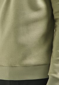 Olivengroene sweatshirt gemaakt van zachte stof, met een geribde zoom en manchetten. Het ontwerp heeft een losse pasvorm en minimale naden.