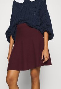 Jersey de punto color azul marino con un patrón texturizado y mangas oversized, combinado con una falda de línea A burgundy de tela suave.