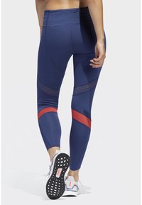 Granatowe legginsy z czerwonymi poziomymi akcentami i panelami z siateczki. Gładka faktura, dopasowany krój, średni stan oraz widoczny pas.