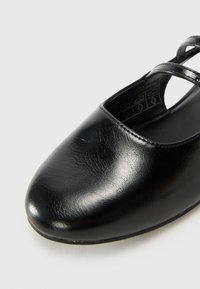 Black leather ballet flat with a smooth finish, rounded toe, and dual thin straps crossing over the top. Flat sole and minimal embellishments.