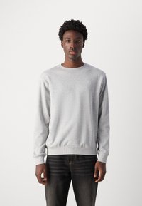 Sudadera gris hecha de una tela suave, con un cuello redondo y puños acanalados, combinada con jeans oscuros. Diseño simple y sin adornos.