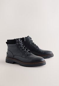 Čierne členkové kožené čižmy s textúrovaným povrchom, zaoblenou špičkou, šnurovaním vpredu, bočným zipsom a kontrastným hnedým detailom na podrážke.