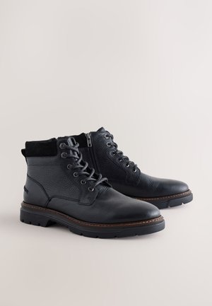 Zwarte leren enkellaarsjes met een gestructureerde afwerking, ronde neus, veters aan de voorkant, zijrits en contrasterend detail van de bruine zool.