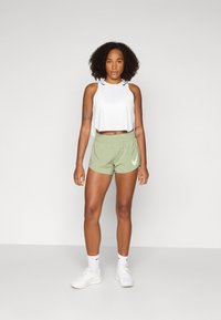 Cropped top bianco con accenti neri, pantaloni corti verde chiaro con logo laterale e scarpe da ginnastica bianche con calze bianche testurizzate.