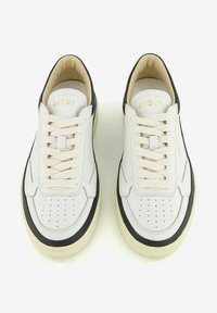 Sneakers bianchi in pelle con accenti neri e suola in gomma color crema. Caratteristiche includono un design della punta perforato e lacci beige. Logo del marchio in oro sulla linguetta.
