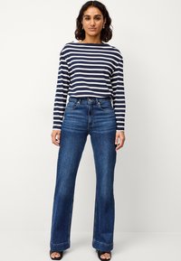 Marineblauw en wit gestreepte langemouwen shirt, gecombineerd met hoge taille donkerblauwe wijde jeans. Gladde stof, relaxte pasvorm en opgerolde zoom.