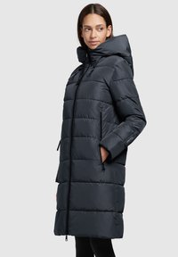 Puffer coat in dark navy. Features a long, quilted design, adjustable hood, front zipper, and side pockets. Smooth, glossy texture.