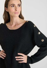 Maglione nero lavorato a maglia con vestibilità ampia, scollo largo e dettagli con bottoni dorati sulle maniche. Texture morbida e caduta relax.