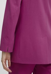 Magenta blazer med en mjuk textur, som har en rak skärning och en delad ärmdetalj, i kombination med matchande byxor som syns längst ner.