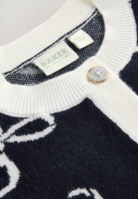 Cardigan in maglia blu navy con colletto a coste bianco, caratterizzato da un motivo floreale e un singolo bottone chiaro. Le etichette sono visibili all'interno.